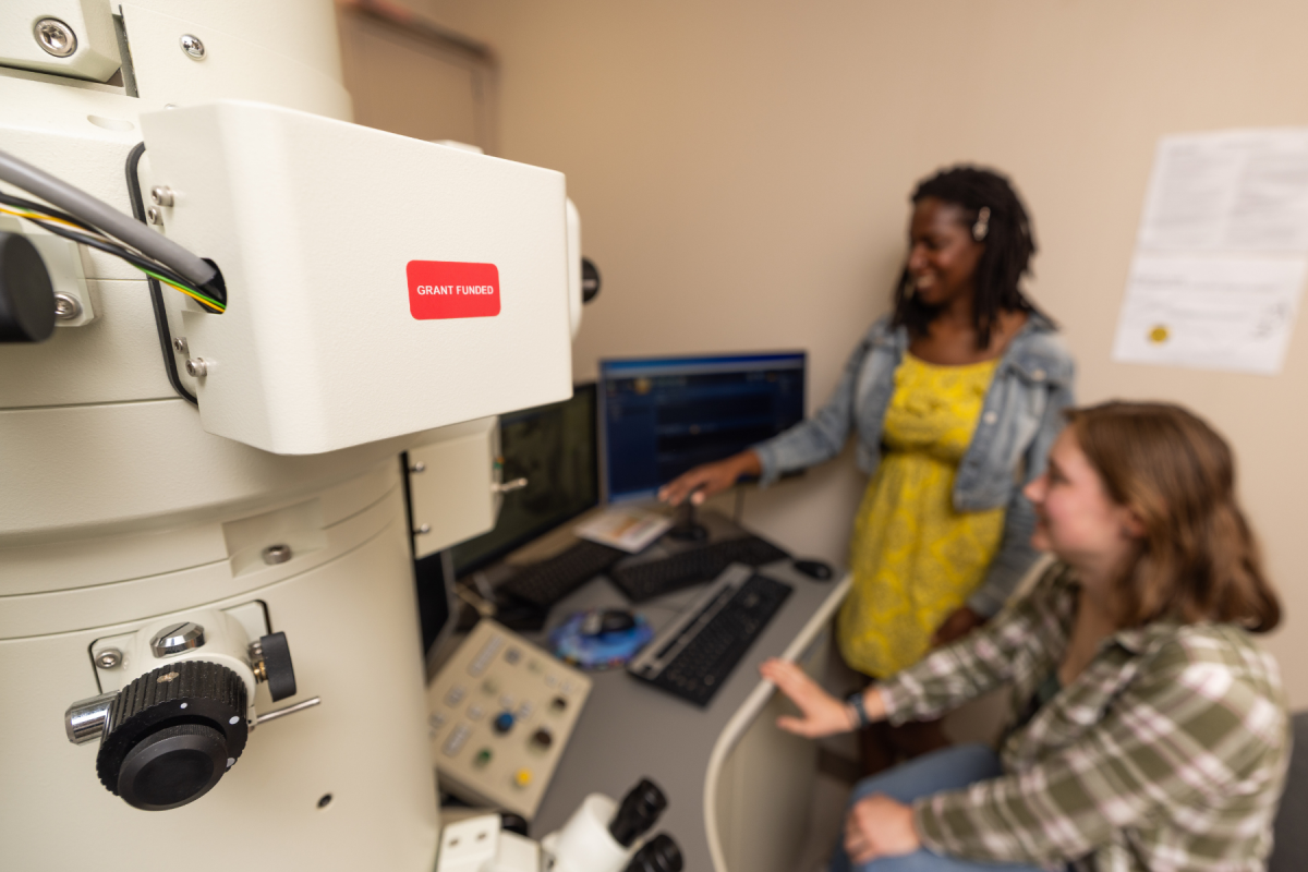 Two women collaborate beside a medical imaging machine and computer console, creating a professional, supportive setting.