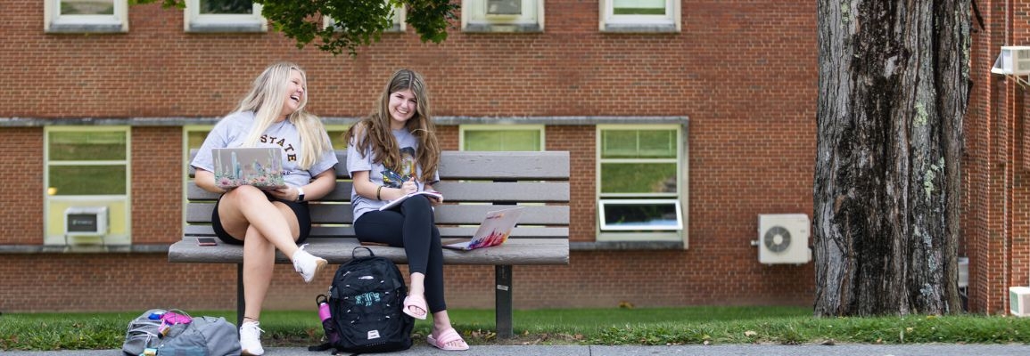 Two students smile while sitting on a bench in front of I.G. Greer.