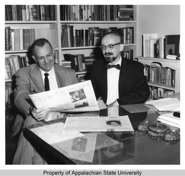 Cratis Williams, professor of English, sitting at a desk beside another man looking at a newspaper at Appalachian State University (1967-current). 