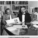 Cratis Williams, professor of English, sitting at a desk beside another man looking at a newspaper at Appalachian State University (1967-current). 