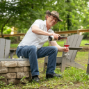 Erik Martella sits on a stone wall and smiles while pouring himself a glass of red wine.