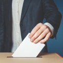A hand placing a ballot in a box. Stock image.