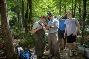 Professor Shea Tuberty, second from left, assists Eli Fried, a student at Chapel Hill High School, with his waders. Andrew Degele, far right, a student at Cardinal Gibbons High School in Raleigh, and Salil Pai, a student in the Early College at Guilford Community College, observe. Photo by Marie Freeman