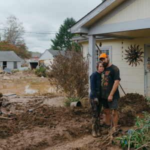 Joe Dancy and Jenna Shaw stand in front of their flooded and mud-filled home in Swannanoa after Hurricane Helene. Photo by Jesse Barber
