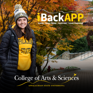 A student in black and gold App State winter gear smiles for a photo in front of the Rankin Science South building.