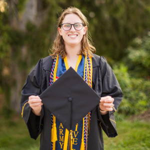 Chloe Lemos, a senior criminal justice major, stands in her cap and gown apparel with five cords at the Founders Bell Pavilion April 13. (Sydney Willis)