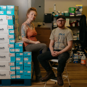 Kimberly Treadaway, left, and Oscar Smith, sit beside a stack of needle boxes at Holler Harm Reduction in Marshall, North Carolina. (Jesse Barber / Grist)