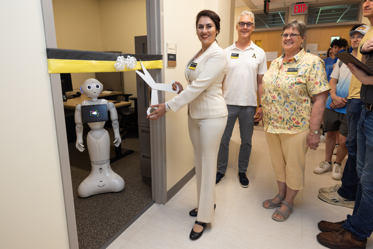 Dr. Yeganeh Madadi (left), assistant professor and director of the Robotics Lab in the Department of Computer Science, cuts the ribbon with Dr. Jay Fenwick, chair of the Department of Computer Science (middle), and Dr. Donna Lillian, associate dean in the College of Arts and Sciences (right), during the Robotics Lab opening on June 25 in Anne Belk Hall. Photo by Chase Reynolds
